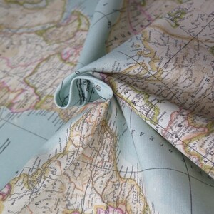 May include: A close-up of a light blue fabric with a vintage world map printed on it. The fabric is folded in a way that shows the map's details, including continents, countries, and oceans.