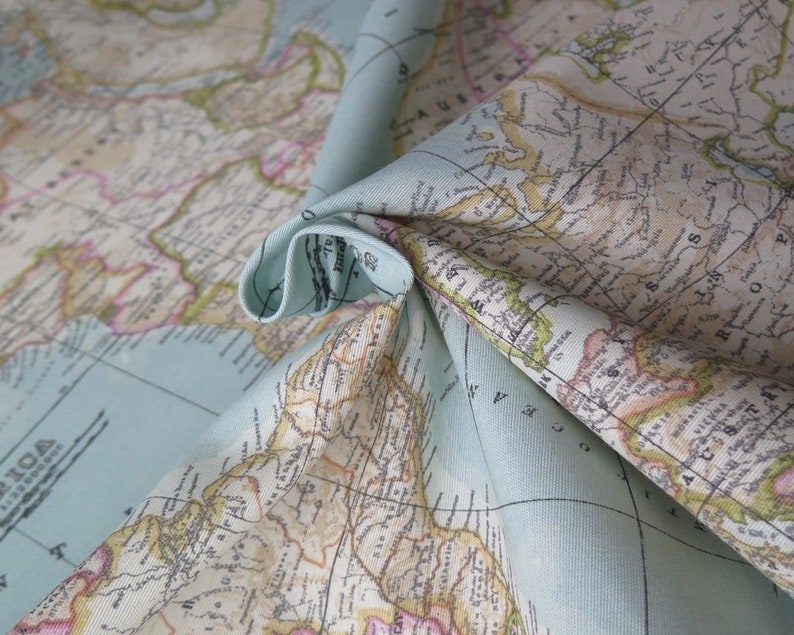 May include: A close-up of a light blue fabric with a vintage world map printed on it. The fabric is folded in a way that shows the map's details, including continents, countries, and oceans.