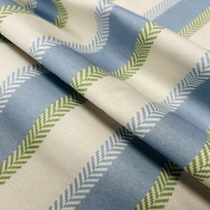 May include: Close-up of a folded fabric with a blue, white, and green striped pattern. The stripes alternate between solid blue and white, with green herringbone accents. The fabric has a soft, textured appearance, suitable for home decor.