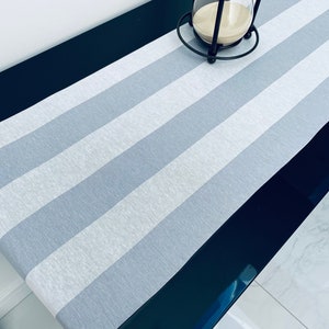 Op de afbeelding: Een grijze en witte gestreepte tafelrunner met een zwarte achtergrond. De runner is gemaakt van een zachte, textuurrijke stof.