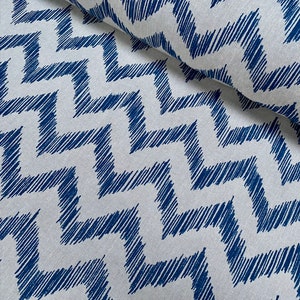 Puede incluir: Tela blanca con un patrón de chevron azul. La tela está tejida con una superficie texturizada, ligeramente rugosa.