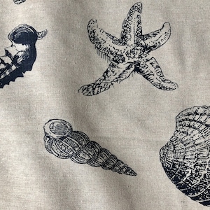 May include: A beige fabric with a black and white print of seashells and a starfish. The fabric has a linen texture.