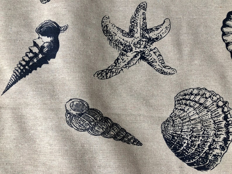 May include: A beige fabric with a black and white print of seashells and a starfish. The fabric has a linen texture.
