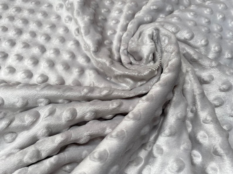 May include: A close-up of a soft, gray, textured fabric with a raised dot pattern. The fabric is folded and draped, showing the texture and the subtle sheen of the material.