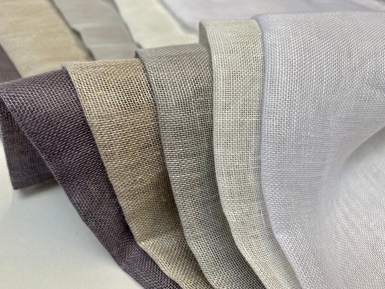 Puede incluir: Primer plano de seis muestras de tela en diferentes tonos de gris, beige y blanco. La tela tiene una textura tejida y un brillo sutil.