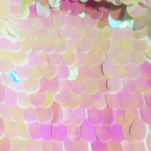 Puede incluir: Primer plano de lentejuelas iridiscentes de color rosa y blanco dispuestas en forma de escamas de pez. Las lentejuelas están cosidas sobre una tela de malla blanca.