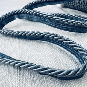 May include: A close-up of a blue braided trim with a satin finish. The trim is thick and has a rope-like texture.