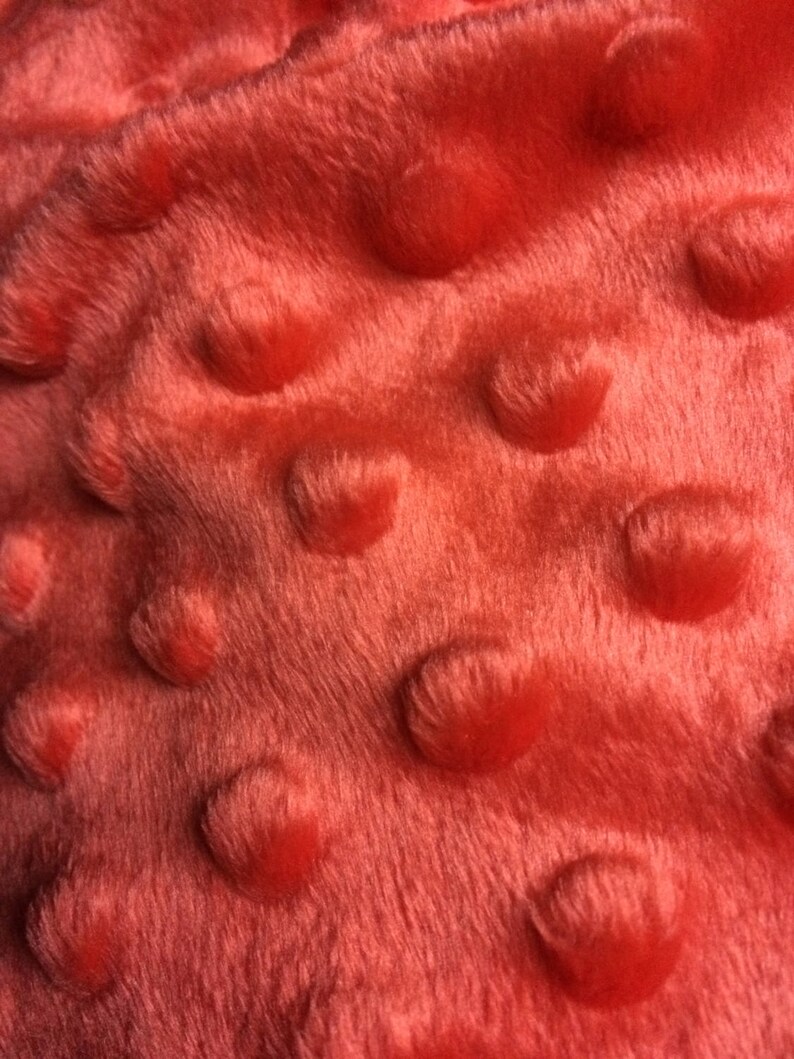 May include: Close-up of a coral-colored minky fabric with a textured, raised dot pattern.