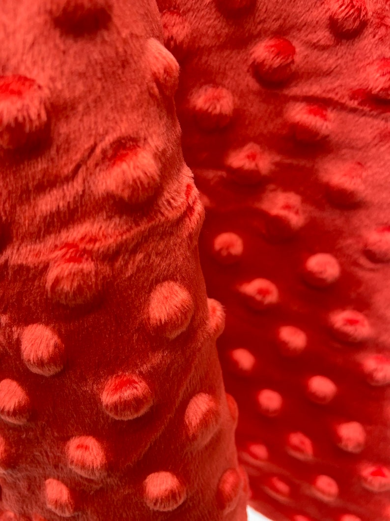 May include: Close-up of a coral-colored minky fabric with a textured, dotted pattern. The fabric is soft and plush, with a subtle sheen.