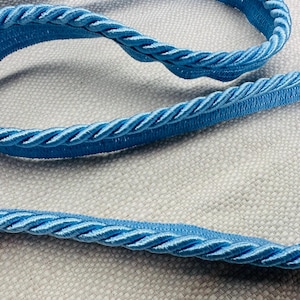 May include: A close-up of a light blue braided trim, perfect for adding a touch of elegance to home decor projects.