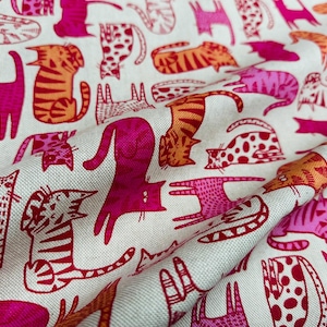Könnte beinhalten: Ein weißer Stoff mit einem sich wiederholenden Muster aus rosa und orangefarbenen Katzen. Die Katzen sind in einem einfachen, cartoonartigen Stil gezeichnet und haben verschiedene Muster auf ihrem Fell.