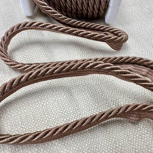 May include: A close-up of a brown braided rope trim. The rope is thick and has a soft, textured look.