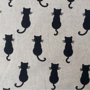 Puede incluir: Una tela beige con un patr&oacute;n repetido de siluetas de gatos negros. Los gatos est&aacute;n mirando hacia adelante con sus colas enroscadas detr&aacute;s de ellos.