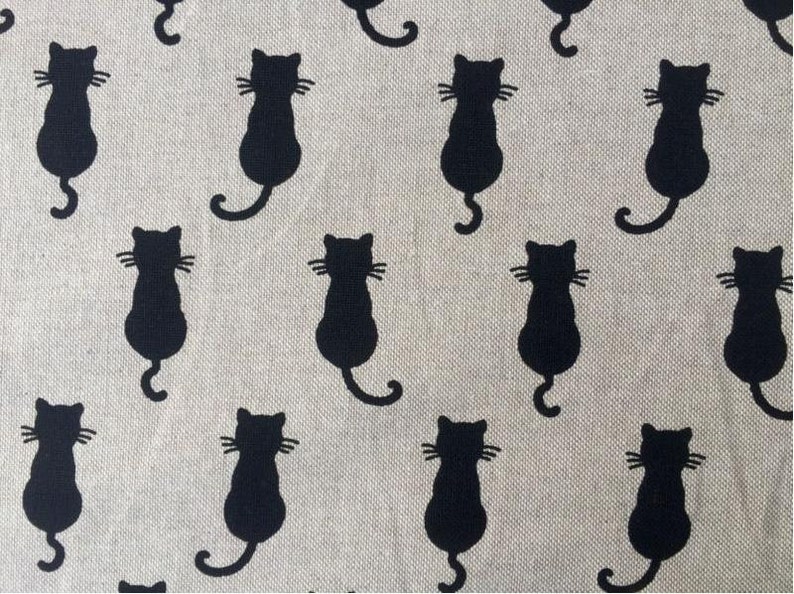 Puede incluir: Una tela beige con un patr&oacute;n repetido de siluetas de gatos negros. Los gatos est&aacute;n mirando hacia adelante con sus colas enroscadas detr&aacute;s de ellos.