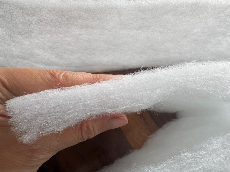 May include: Close-up of a handful of fluffy, white polyester fiberfill. The material is soft and cloud-like, ideal for stuffing pillows, cushions, or craft projects. The texture is visible, showing the individual fibers.