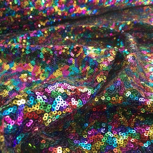 May include: Close-up of a fabric covered in iridescent sequins in a variety of colours, including red, green, blue, purple, and gold.