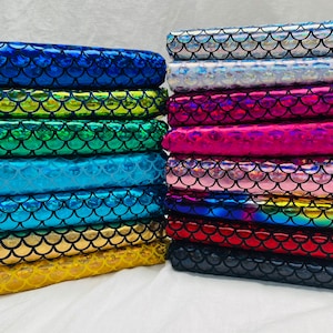 Puede incluir: Una pila de tela de escamas de sirena iridiscente en varios colores, incluyendo azul, verde, rosa y plateado. La tela está dispuesta en una pila ordenada, mostrando las escamas brillantes.