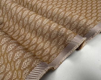 May include: Close-up of a folded fabric with a repeating pattern of white leaf-like shapes on a brown background. The edge of the fabric has a striped border in brown and white.