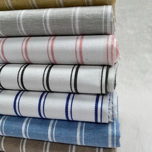 May include: A stack of striped fabric in various colors, including beige, gray, pink, white, blue, and brown. The fabric is folded and stacked neatly.