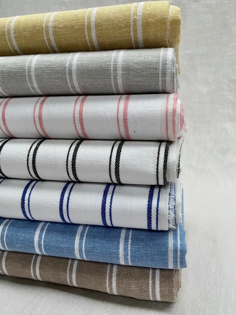 May include: A stack of striped fabric in various colors, including beige, gray, pink, white, blue, and brown. The fabric is folded and stacked neatly.