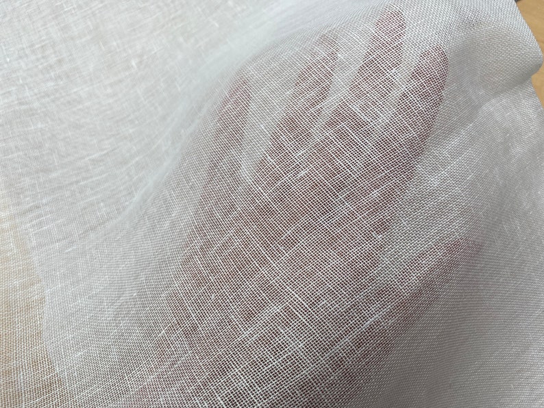 May include: White sheer fabric with a woven texture. The fabric is lightweight and translucent.