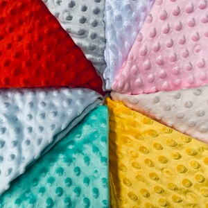 May include: A collection of eight fabric swatches in various colors, including red, pink, light blue, yellow, and teal. Each swatch has a textured, raised dot pattern.