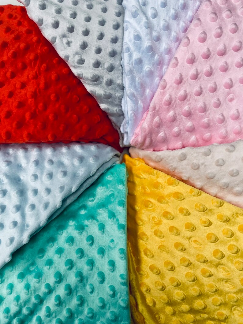 May include: A collection of eight fabric swatches in various colors, including red, pink, light blue, yellow, and teal. Each swatch has a textured, raised dot pattern.