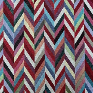 Könnte beinhalten: Nahaufnahme eines bunten Stoffes mit Chevron-Muster. Der Stoff besteht aus gewebten Fäden in Rot-, Blau-, Grün-, Weiß- und Schwarztönen.
