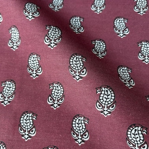 Puede incluir: Primer plano de una tela burdeos con un estampado de cachemira repetido. El diseño de cachemira presenta una combinación de colores blanco y marrón, creando un aspecto clásico y elegante. La tela tiene un ligero brillo, lo que sugiere una textura suave.