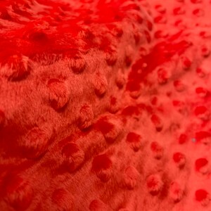 May include: Close-up of a bright orange fabric with a textured, raised dot pattern. The fabric is soft and plush.