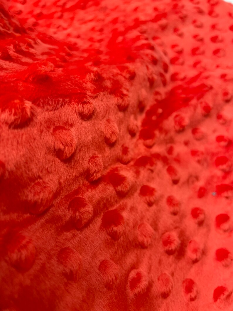 May include: Close-up of a bright orange fabric with a textured, raised dot pattern. The fabric is soft and plush.