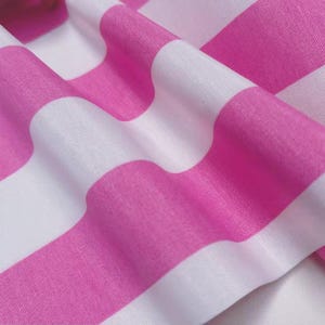 May include: Close-up of a fabric with alternating wide pink and white stripes. The fabric is folded, creating soft curves and shadows. The bright pink color contrasts with the white, creating a visually appealing pattern.
