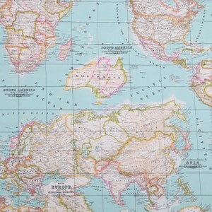 May include: A vintage world map with a light blue background and grid lines. The continents are outlined in brown and filled with different colors. The map includes the names of continents and oceans. The map is printed on paper.
