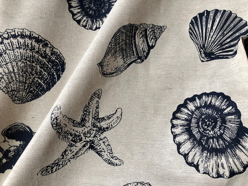 May include: A beige fabric with a black and white print of seashells and a starfish. The fabric has a linen texture.