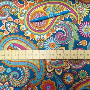 May include: A blue fabric with a paisley pattern in shades of orange, yellow, pink, and green. A ruler is placed on the fabric, with the numbers 1 through 30 visible. The text "BARCLAY" is visible on a blue pen lying on the fabric.