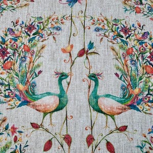 Op de afbeelding: Decoratieve stof met een symmetrisch ontwerp van twee pauwen. De vogels zijn turquoise en perzik, omgeven door kleurrijke bloemen en veermotieven op een neutrale achtergrond.
