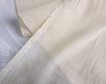 May include: Close-up of a plain, off-white fabric with a subtle texture. The fabric is smooth and appears to be woven.