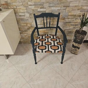 Op de afbeelding: Een donker marineblauwe houten fauteuil met een gebogen rugleuning voorzien van drie verticale spijlen. De zitting is bekleed met een stof met een herhalend geometrisch patroon van afgeronde rechthoekige vormen in tinten tan, zwart en cr&egrave;me.