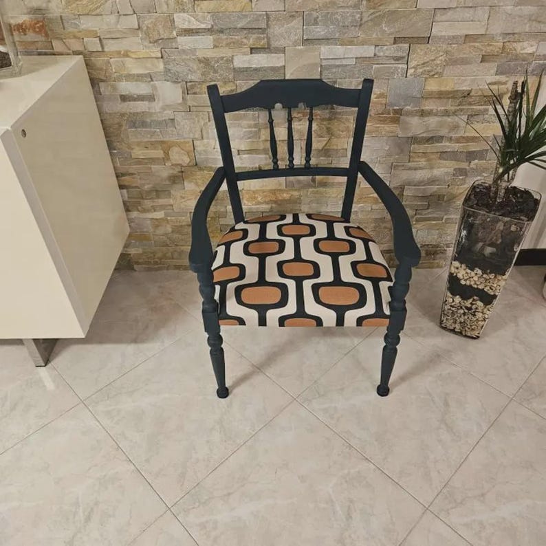 Op de afbeelding: Een donker marineblauwe houten fauteuil met een gebogen rugleuning voorzien van drie verticale spijlen. De zitting is bekleed met een stof met een herhalend geometrisch patroon van afgeronde rechthoekige vormen in tinten tan, zwart en cr&egrave;me.