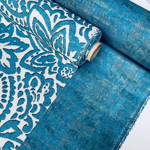 May include: A roll of teal fabric with a white and teal paisley pattern. The fabric is folded in half and the roll is on top of a flat piece of the same fabric.
