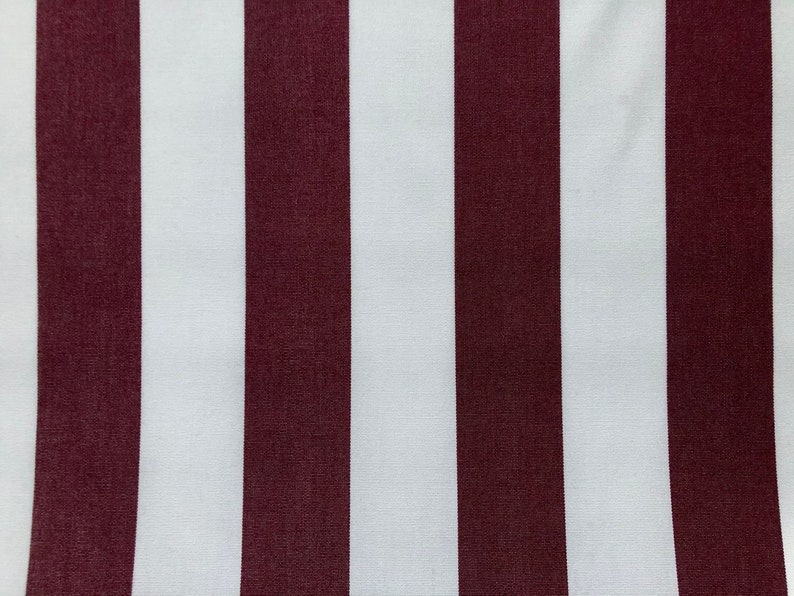May include: Close-up of a fabric with vertical stripes. Alternating wide stripes of white and burgundy create a bold pattern. The fabric appears to be smooth and possibly used for upholstery or home decor.