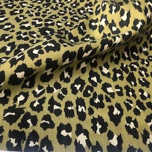 May include: Close-up of fabric with a leopard print pattern. The fabric has a khaki green background with black and white spots. The fabric is folded, showing the texture and pattern.