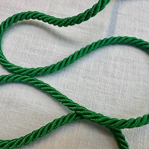 May include: A vibrant emerald green twisted cord made of multiple strands wound together. The rope features a smooth, shiny texture with a consistent spiral pattern throughout its length, creating a decorative trim suitable for various craft projects.