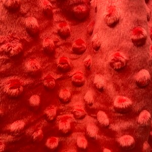 May include: Close-up of a coral-colored fabric with a textured, raised dot pattern. The fabric is soft and plush.
