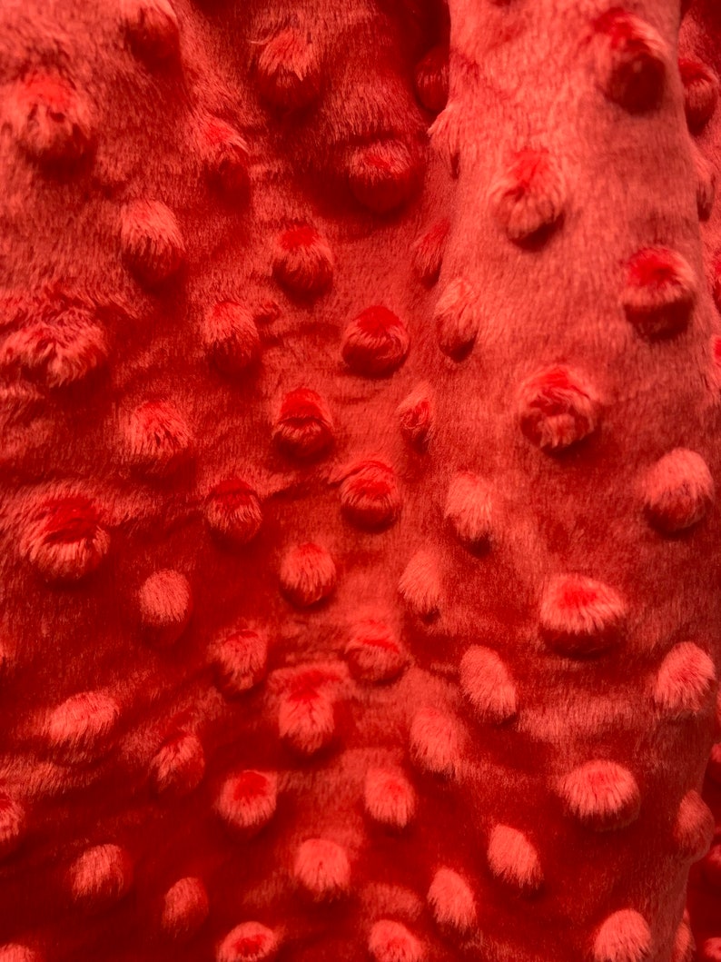 May include: Close-up of a coral-colored fabric with a textured, raised dot pattern. The fabric is soft and plush.