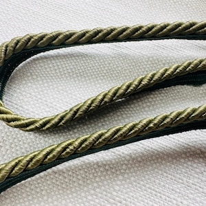 Könnte beinhalten: Nahaufnahme eines geflochtenen Seilschmucks in Grün und Olivgrün. Das Seil ist verdreht und hat einen dezenten Glanz.