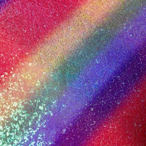 Può includere: Un tessuto di paillettes arcobaleno con un motivo diagonale. Il tessuto è realizzato con paillettes iridescenti in tonalità di rosso, arancione, giallo, verde, blu, indaco e viola.