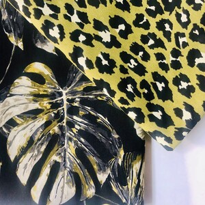 May include: Black fabric with a large white and gold tropical leaf print. The fabric is folded over a green and black leopard print fabric.