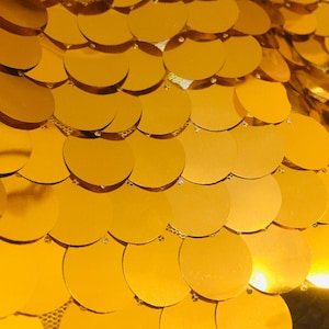 May include: A close-up of a gold fabric with a pattern of overlapping circles. The fabric is shiny and reflective.
