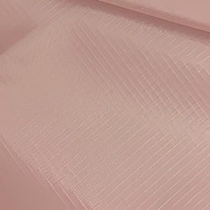 Könnte beinhalten: Nahaufnahme einer strukturierten, blassrosa Oberfläche mit einem diagonalen Gittermuster. Die Oberfläche hat einen subtilen Glanz, und die Linien erzeugen ein Gefühl von Tiefe und Dimension. Der Gesamteffekt ist weich und elegant.